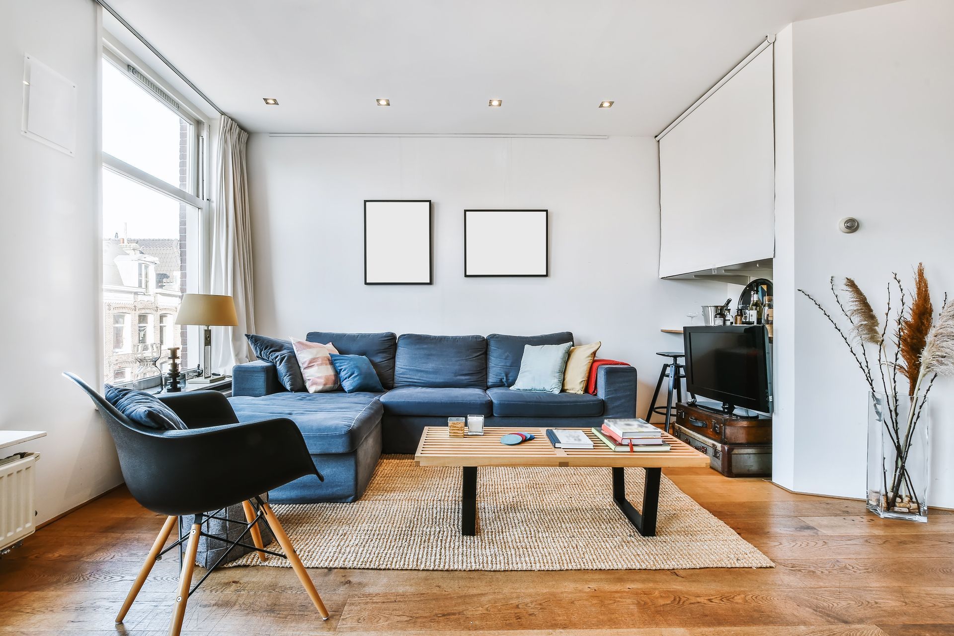 A modern living room with a blue sectional sofa, a wooden coffee table, a black chair, and two framed wall pictures.