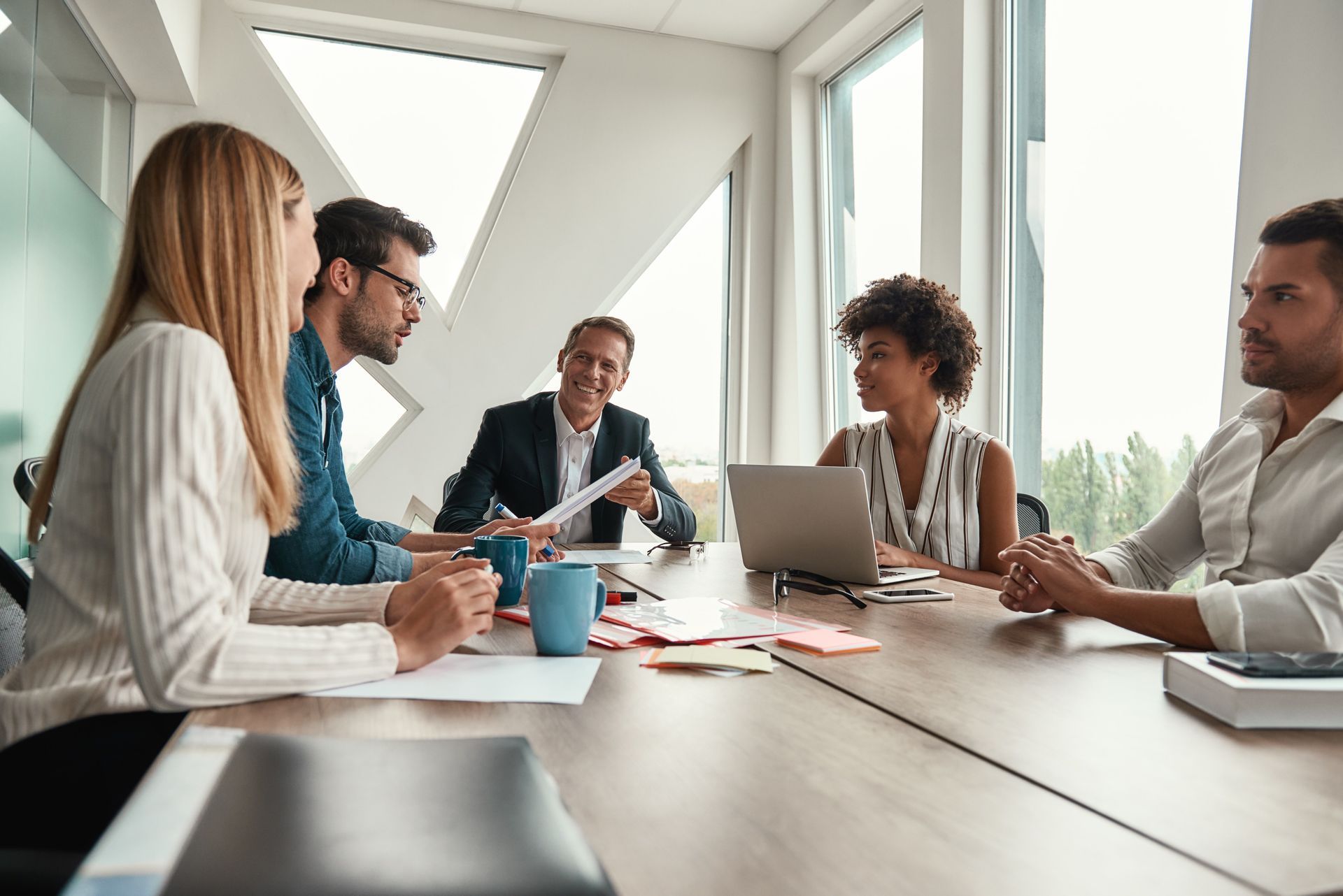 Five people sit around a wooden table in a bright, modern office, engaged in a collaborative meeting.