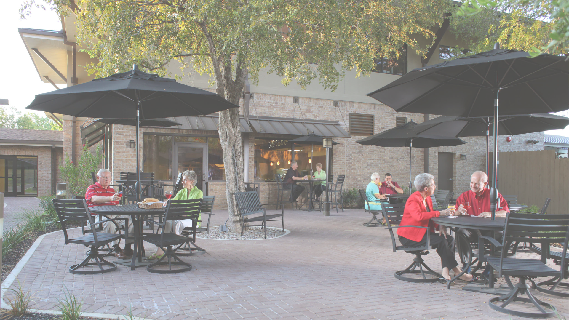 Seniors sitting at tables under umbrellas outside of a senior community living