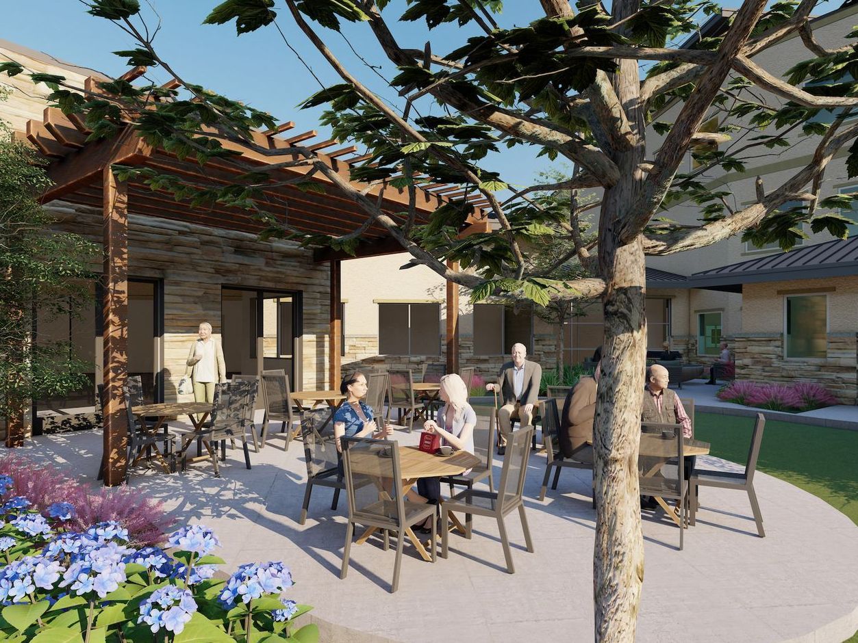 A group of people are sitting at tables under a pergola at a senior care center.