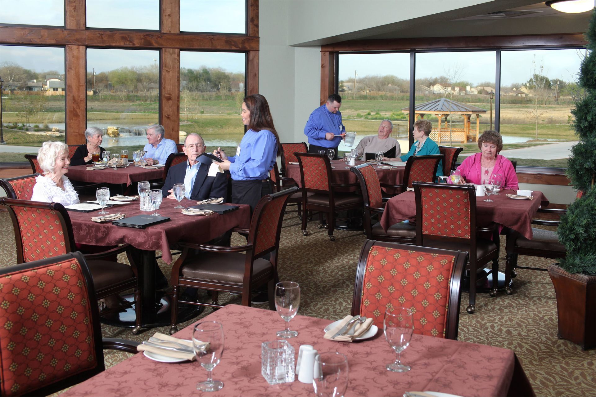 Guests dining in a restaurant with red patterned chairs and large windows overlooking a landscape