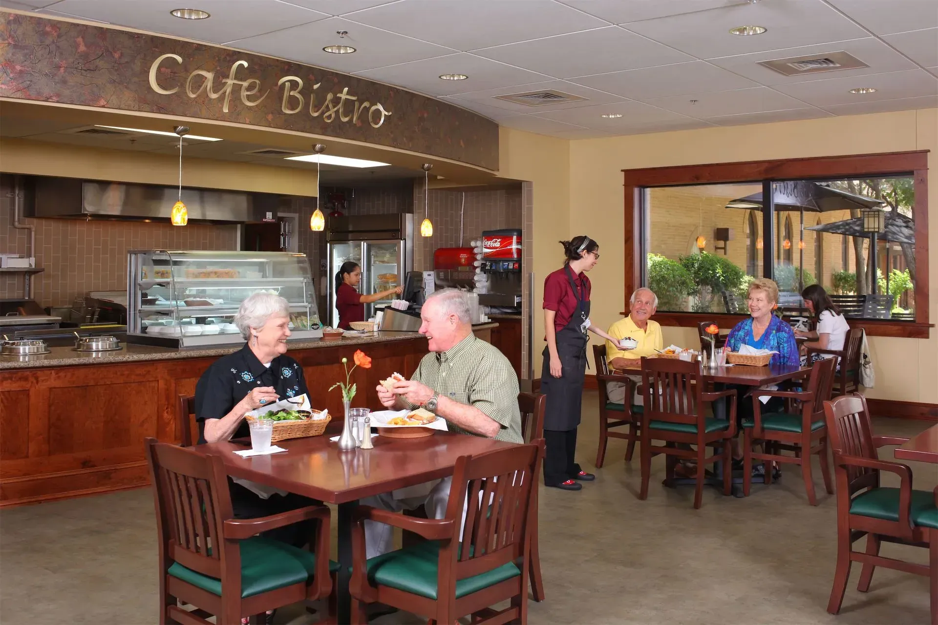 Guests dining in a restaurant with red patterned chairs and large windows overlooking a landscape