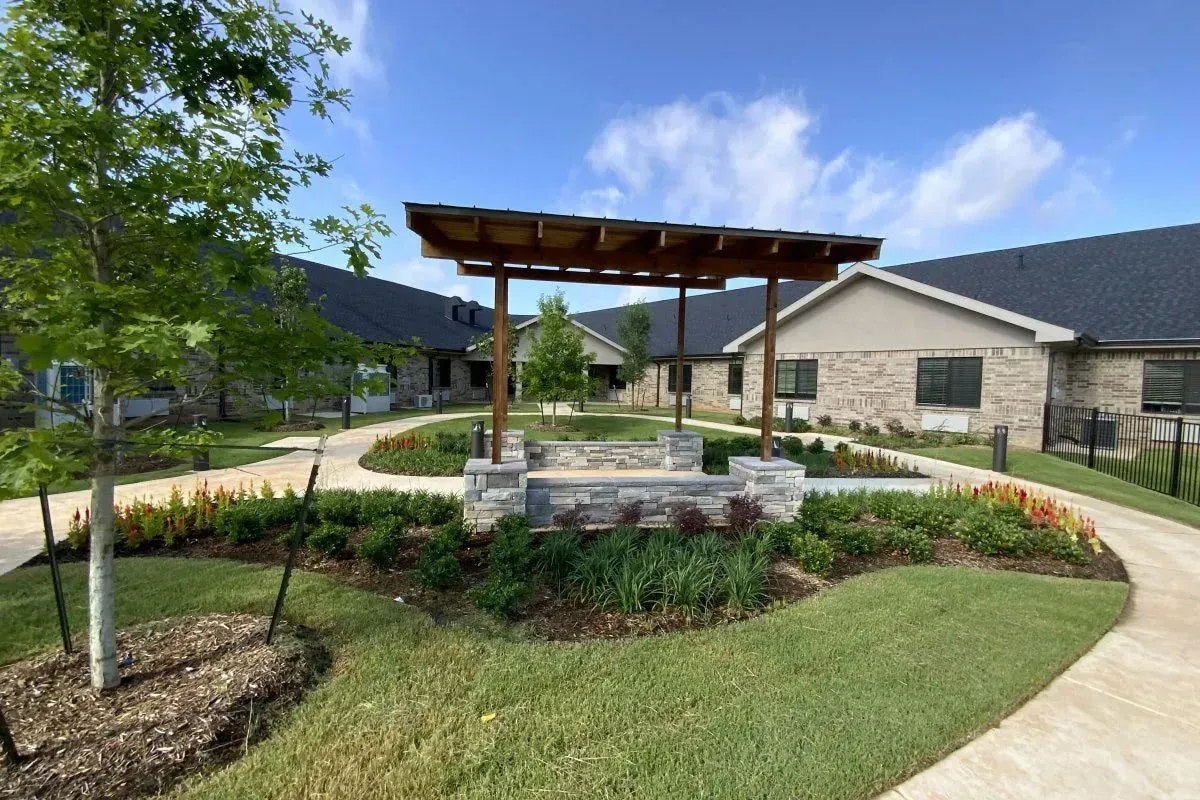 Landscaped courtyard with a wooden pergola, stone benches, and brick buildings under a blue sky