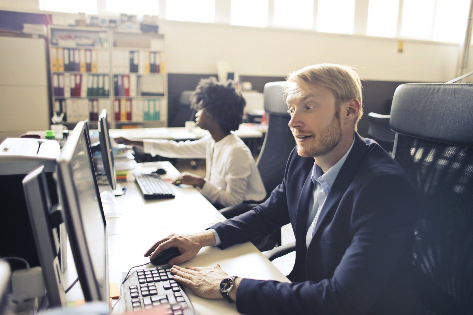 A man and a woman are sitting at a desk in front of a computer.