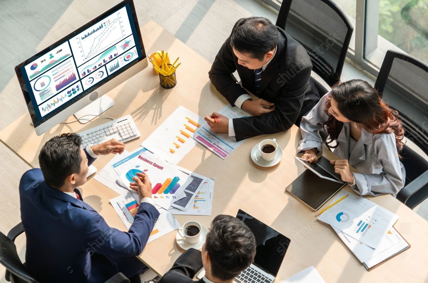 Business team reviewing data charts around a table, discussing, with coffee.