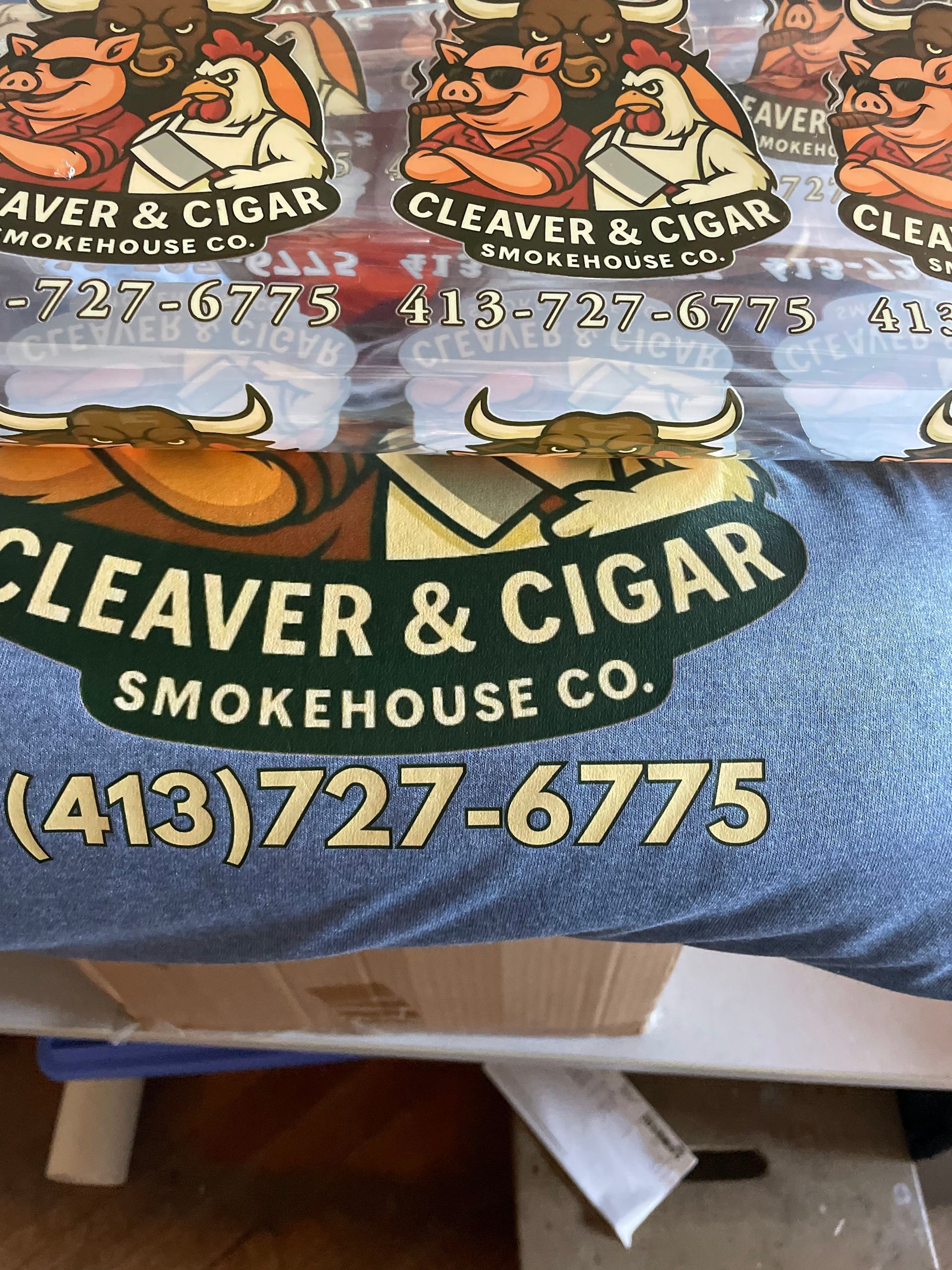 Logo for Cleaver & Cigar Smokehouse Co. featuring a bull, pig, and chicken with the phone number (413) 727-6775.