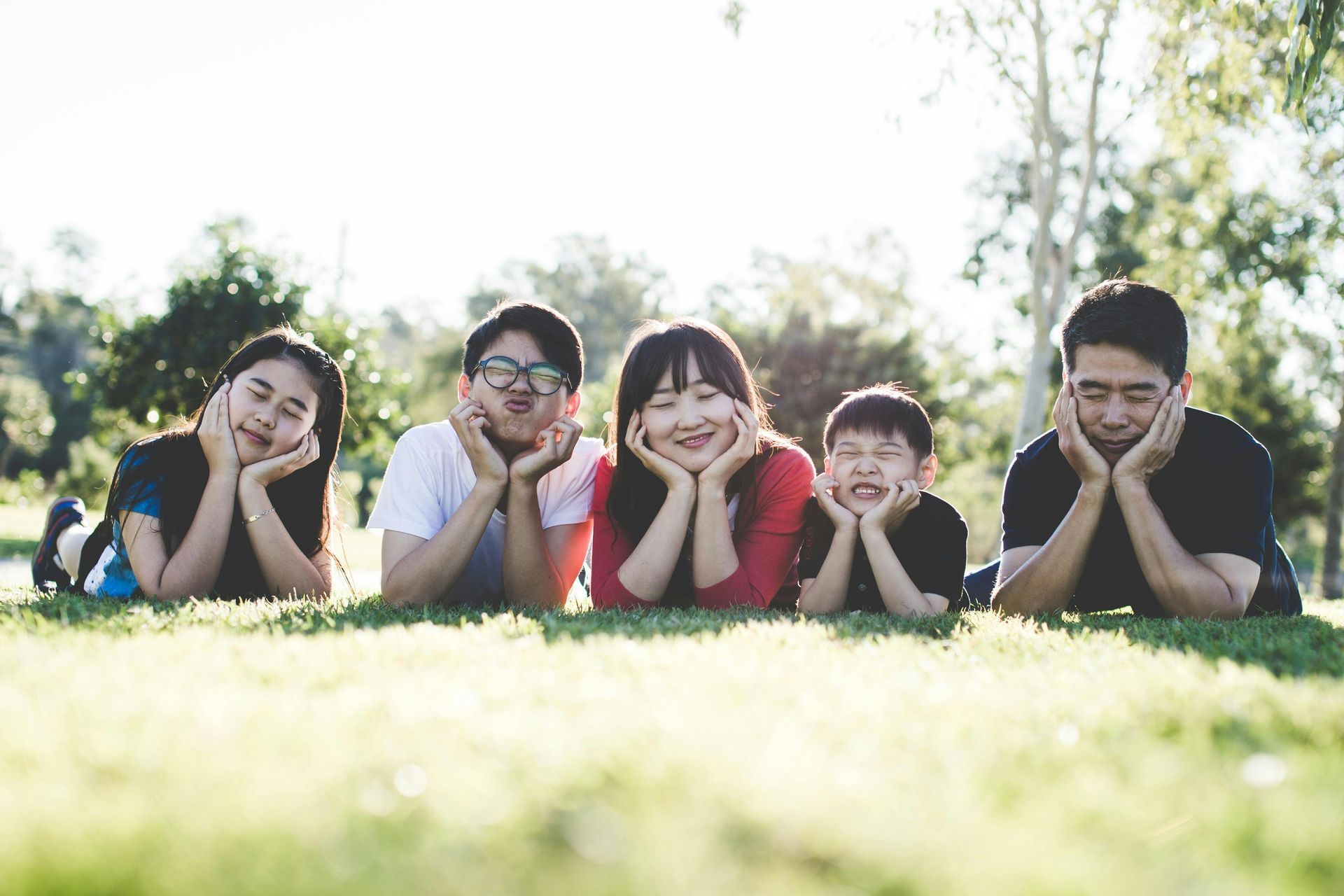 Family lying on grass with hands under chin.