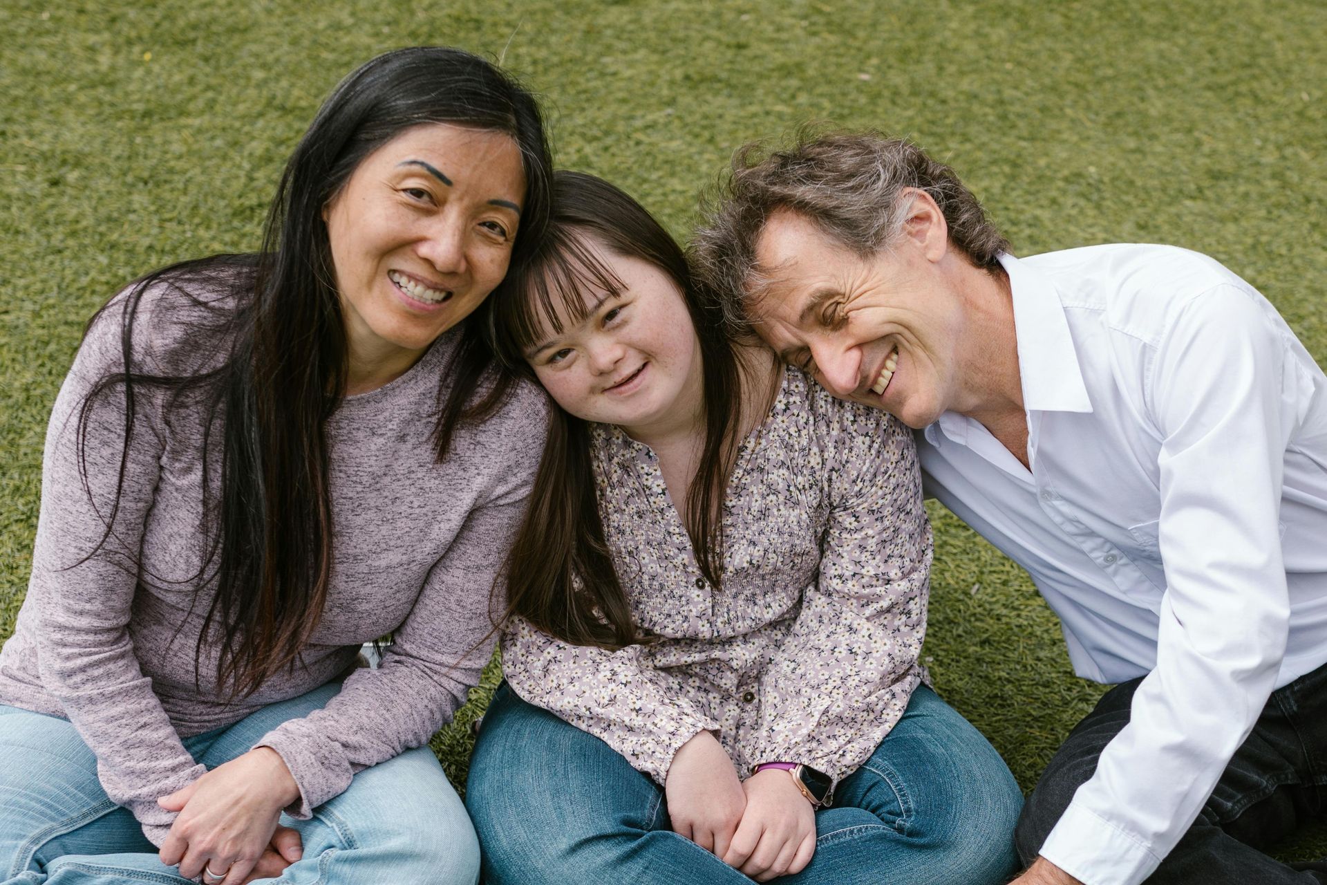 A family with mom, dad and daughter sitting on the grass and smiling.
