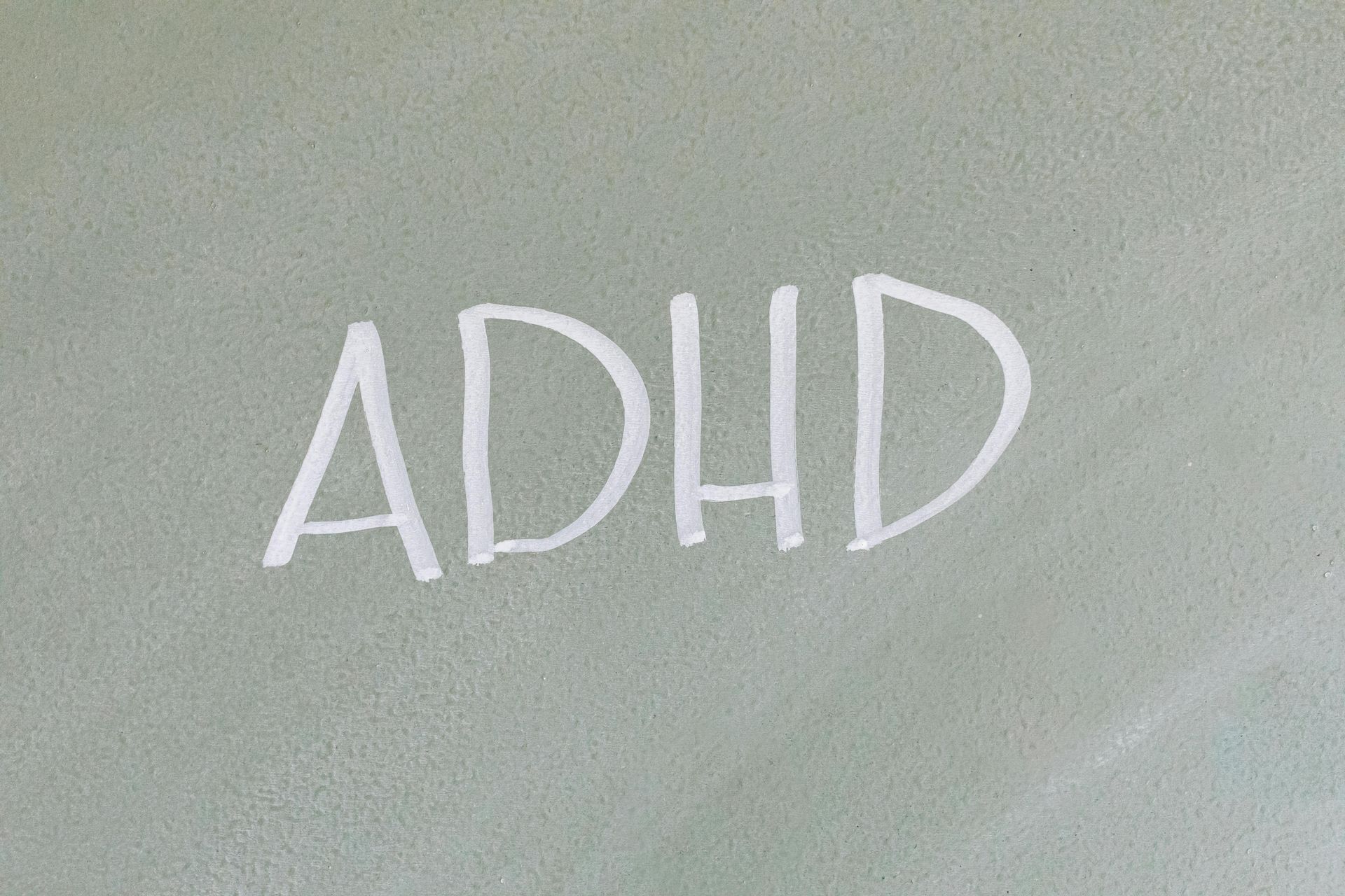 The word ADHD is written in white chalk on a gray surface.