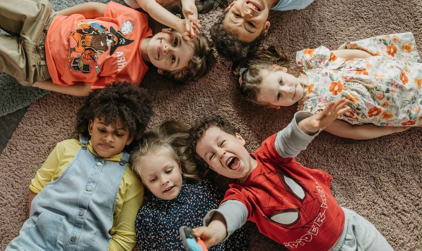 Children lying down on a rug in a circle. 
