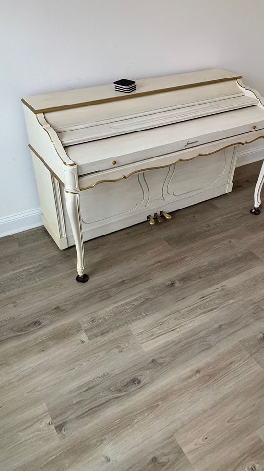 A white piano is sitting on a wooden floor in a room.