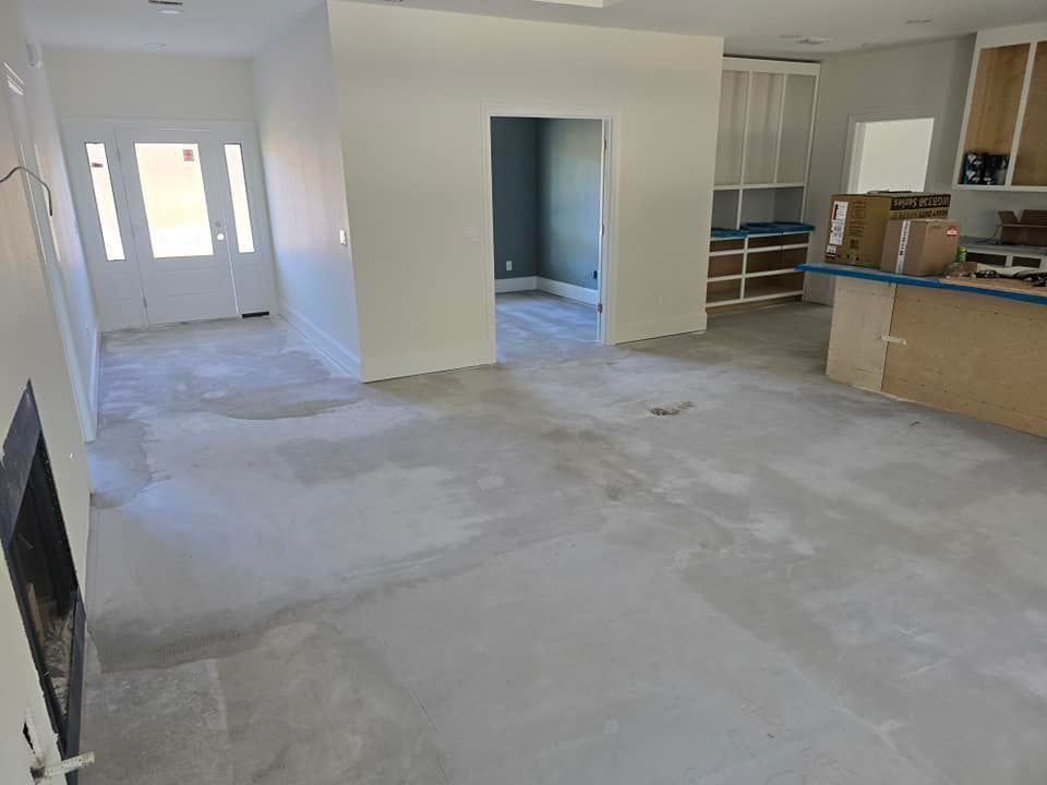 A living room with a concrete floor and a kitchen in the background.