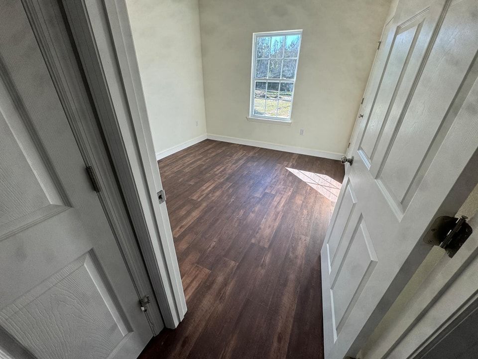 A bedroom with hardwood floors and a window.