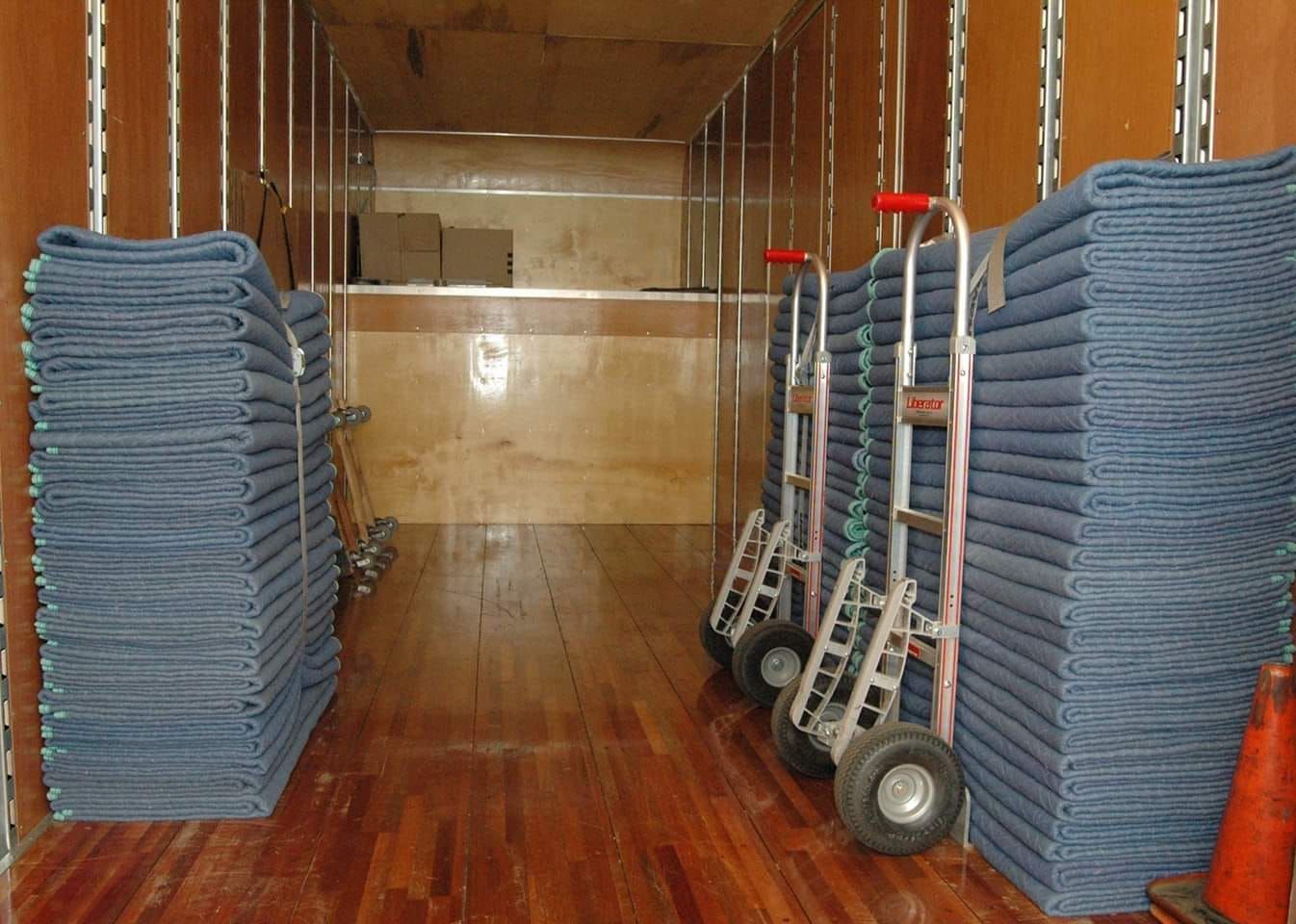 Inside of a moving truck with stacks of blue moving pads and hand trucks.