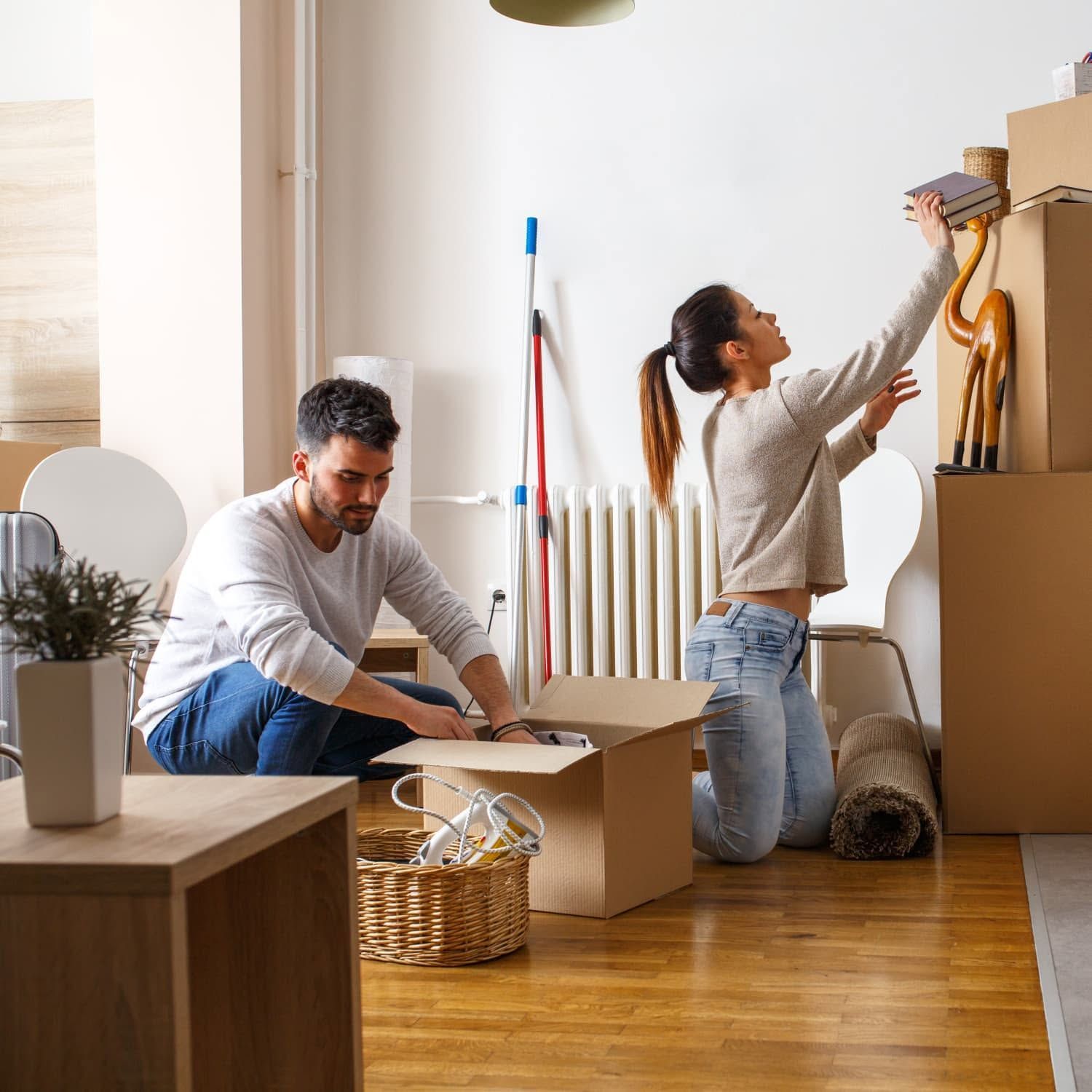 Family unpacking boxes in a new home, a toddler looking at a paper with parents, surrounded by packed boxes.