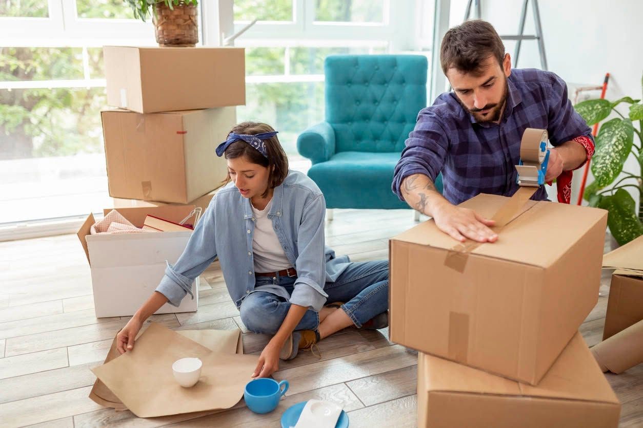 Family unpacking boxes in a new home, a toddler looking at a paper with parents, surrounded by packed boxes.