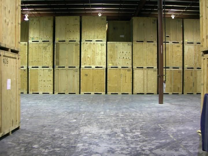 Storage facility interior with rows of wooden storage units stacked high. Concrete floor and dark ceiling.