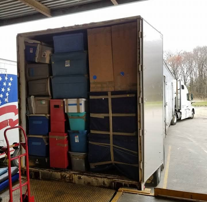 Two movers in blue shirts moving furniture inside a light-filled room.