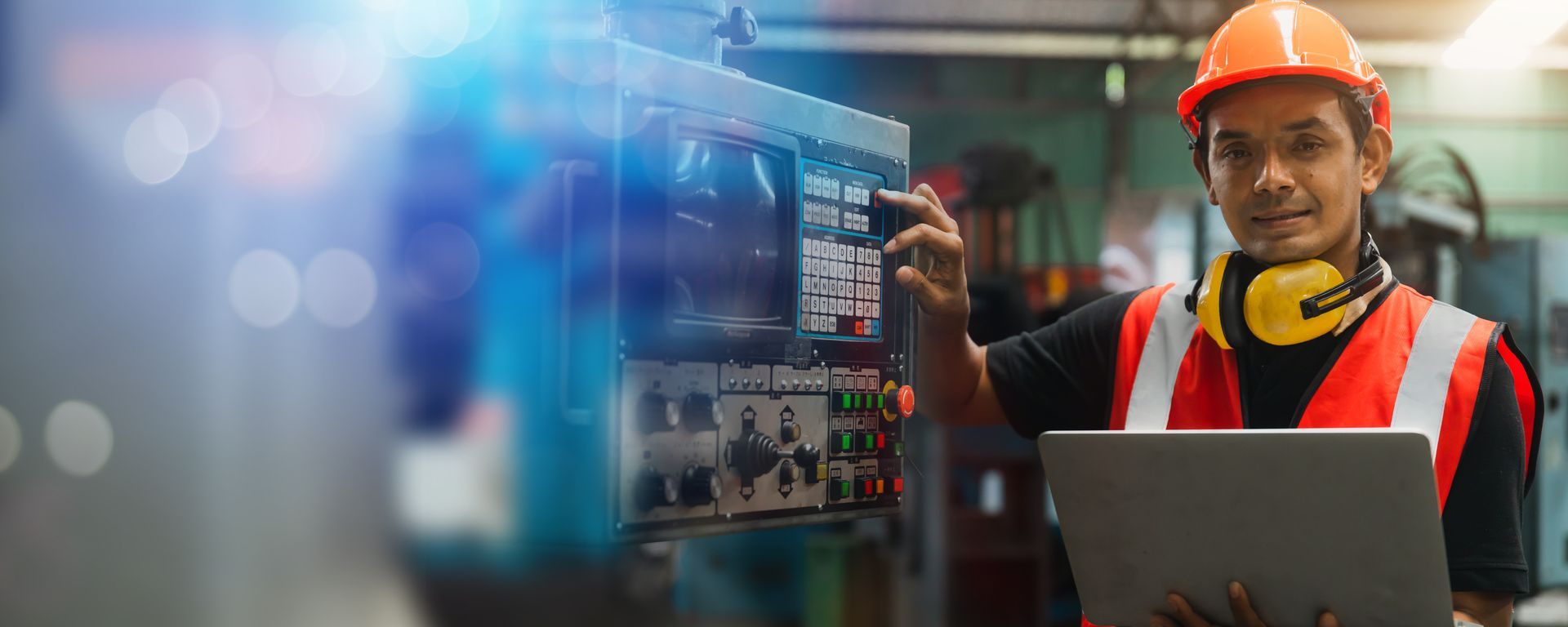 Courageous cultures instill psychological safety and improve performance. Industrial employee working at a machine control panel in an orange hardhat and vest