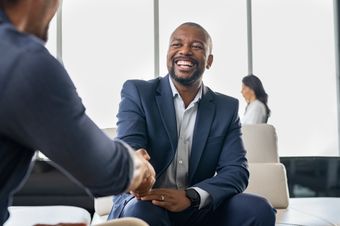 Two employees sitting and shaking hands. One appears to be congratulating the other. Performance feedback makes a great difference.