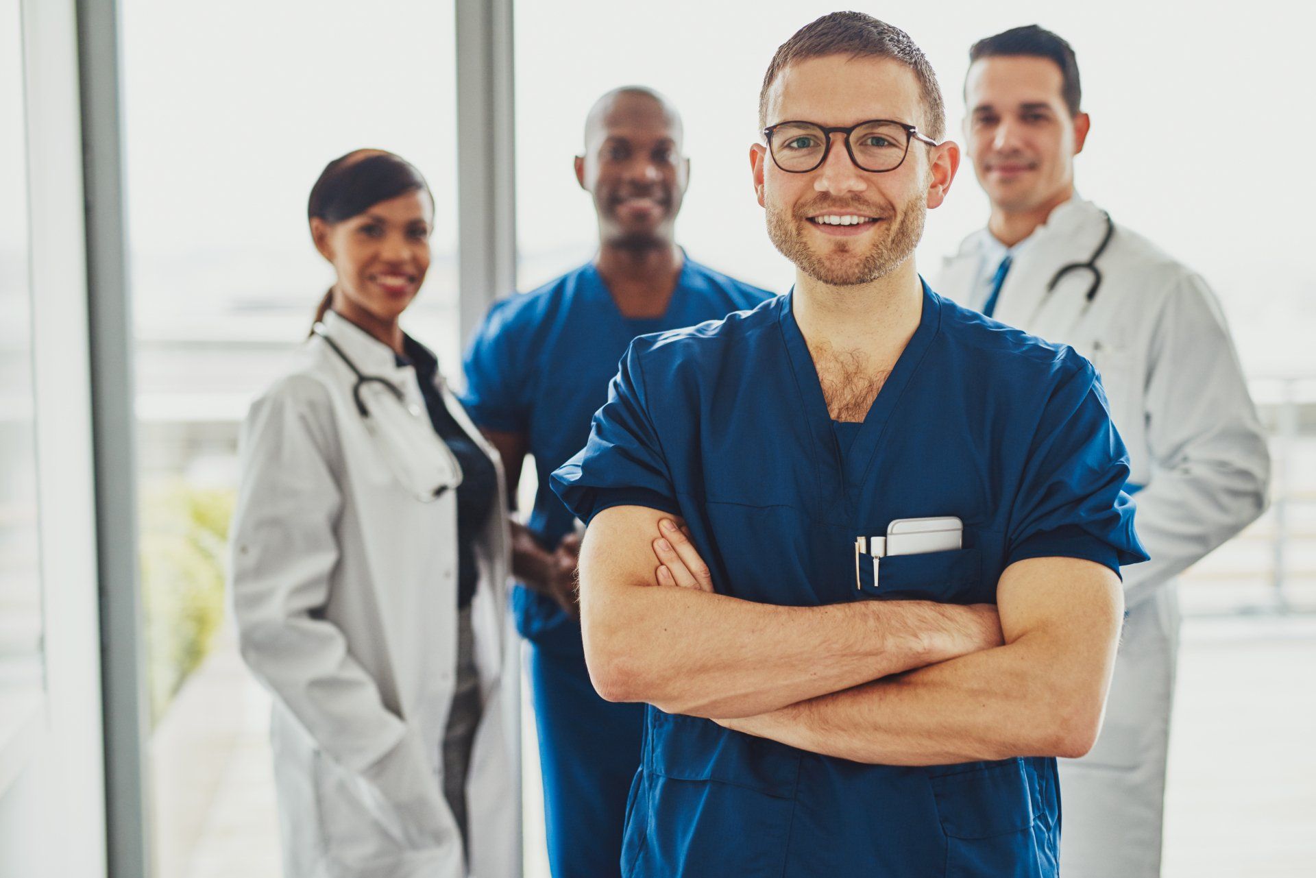 Four medical practitioners standing in front of a brightly lit window, confident and positive.