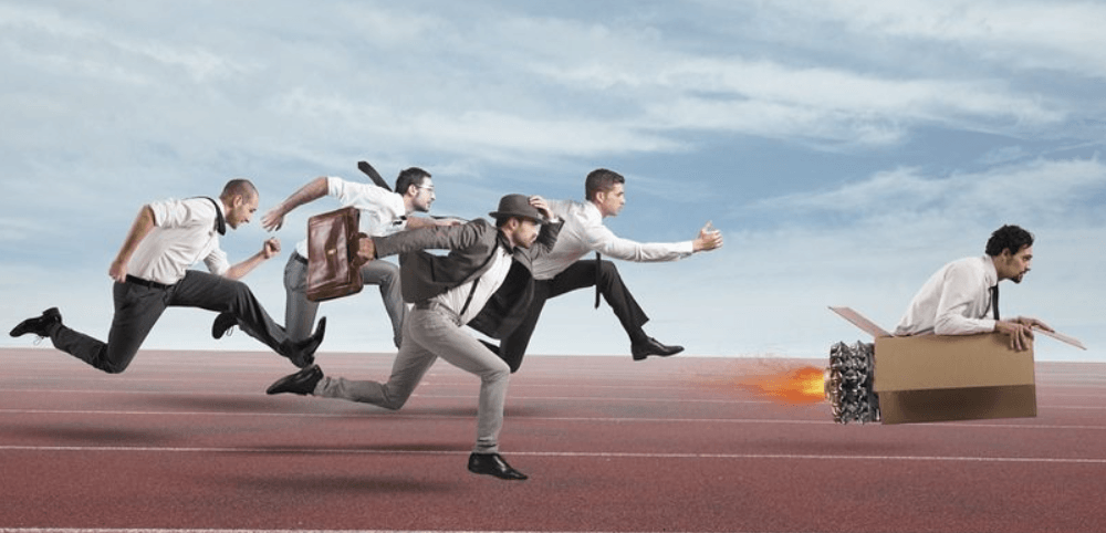 Clarifying the win (your vision) empowers your employees to move achieve it with greater consistency. Artistic rendering of four business people chasing after a fifth business person who is sitting in a cardboard box powered by a jet engine.