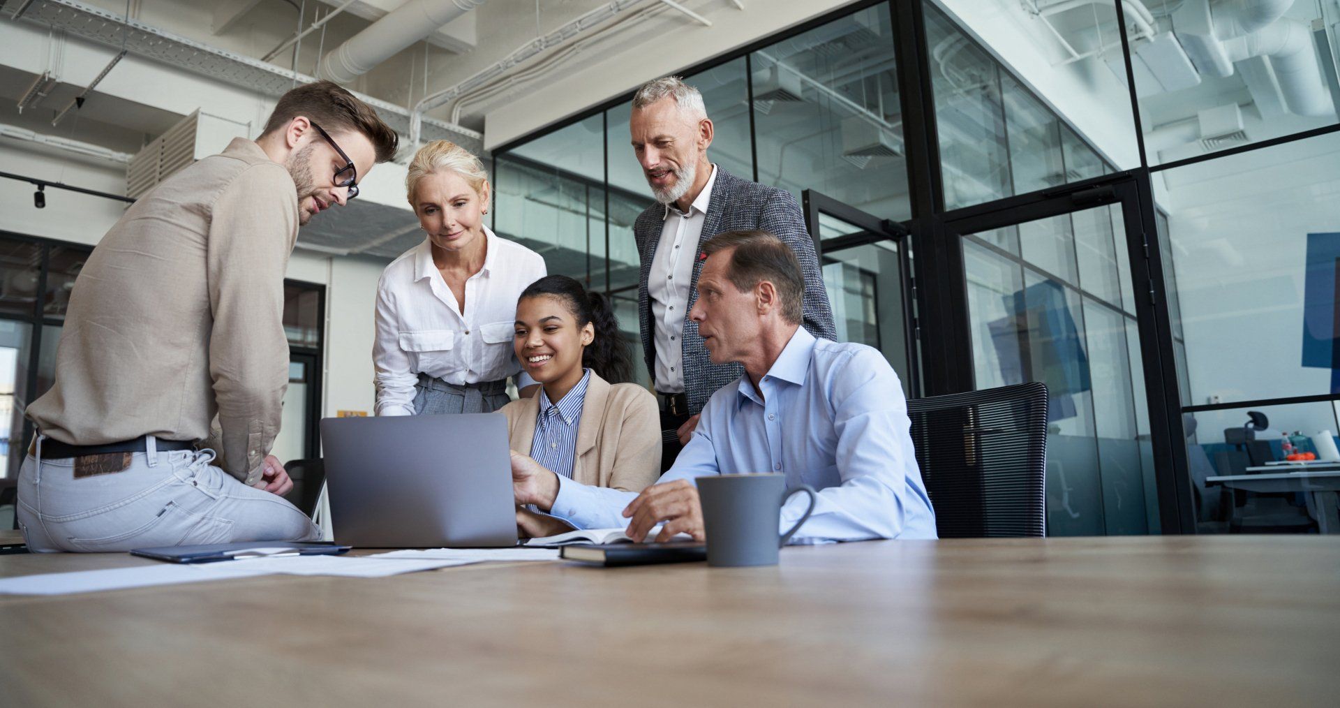 Performance and cohesion start with a winning HR strategy. Team of five employees gathered around a conference room table having a positive discussion.