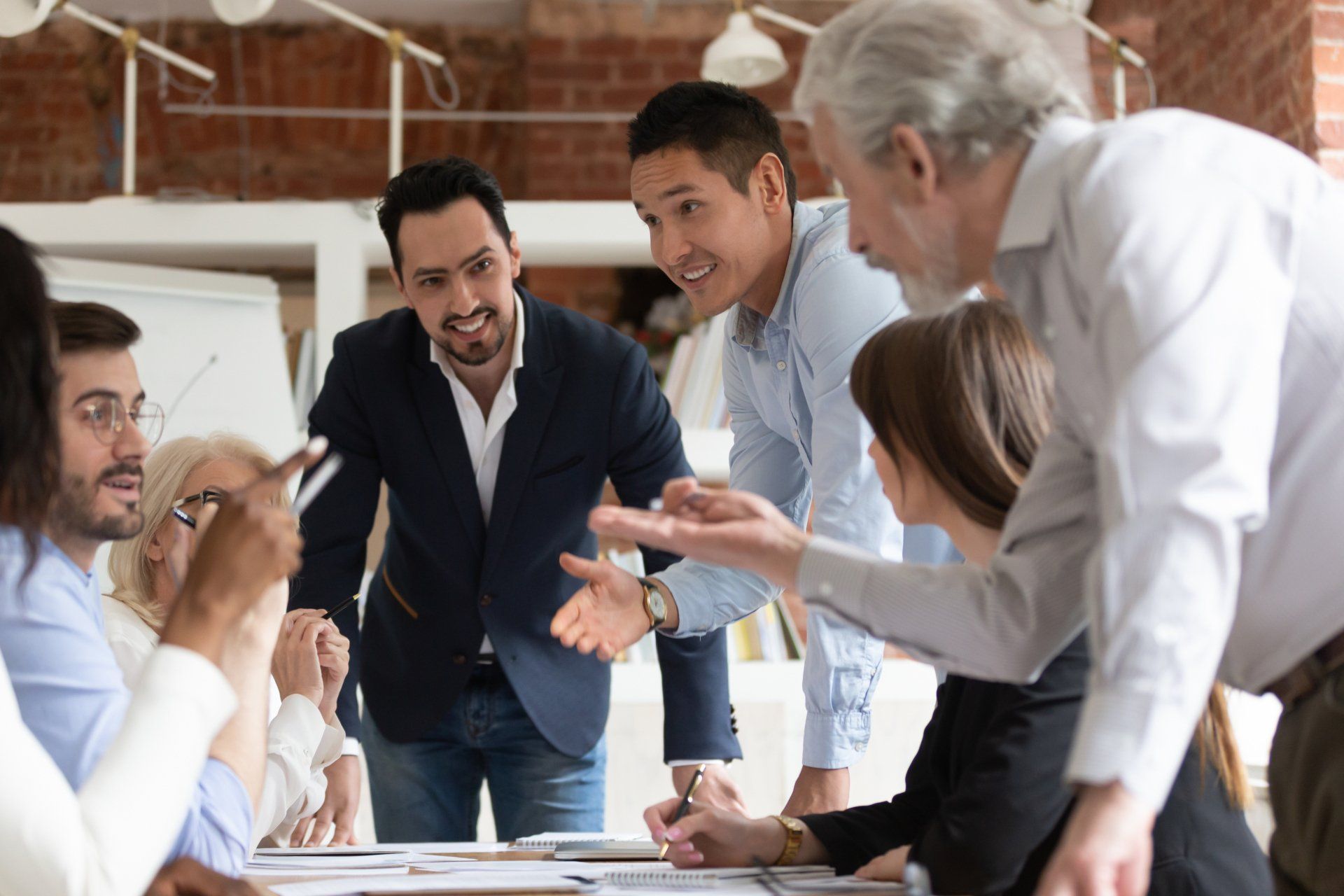 Here are nine common denominators from the most effective teams. Seven employees gathered around conference room table in an energeized discussion.