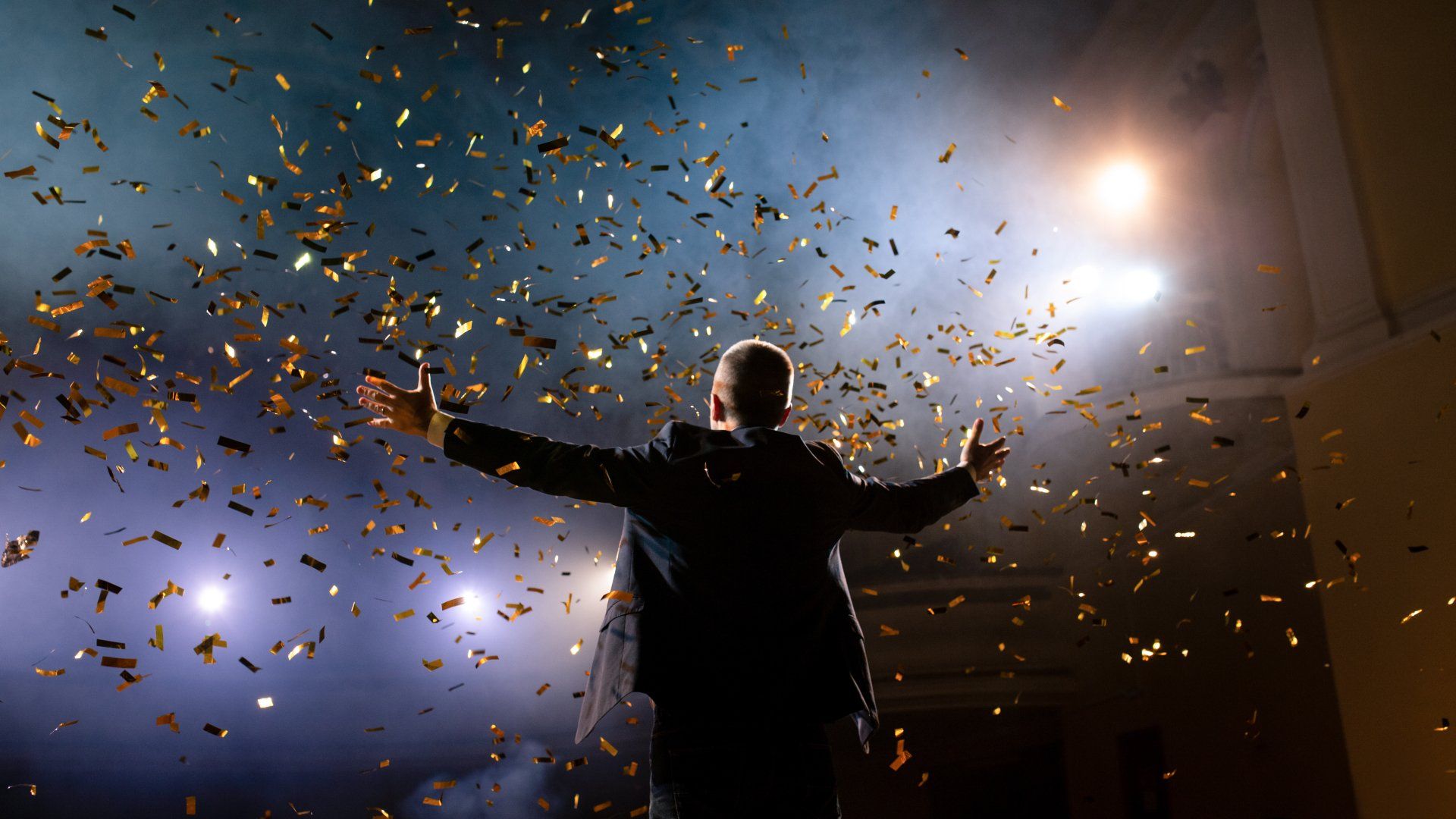 Encourage personal growth - for you and your team. Man standing on stage in front of bright lights with confetti flying.