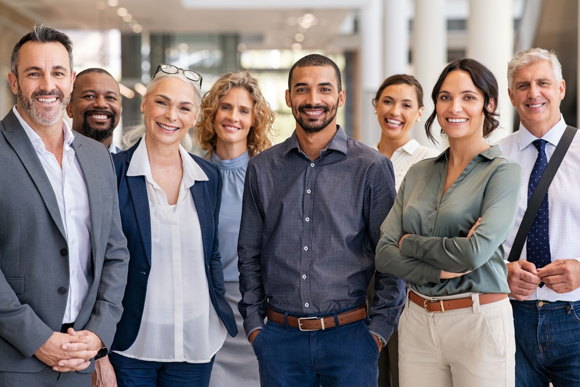 Alignment creates a cohesive team. Eight diverse employees standing together and smiling in an office building.