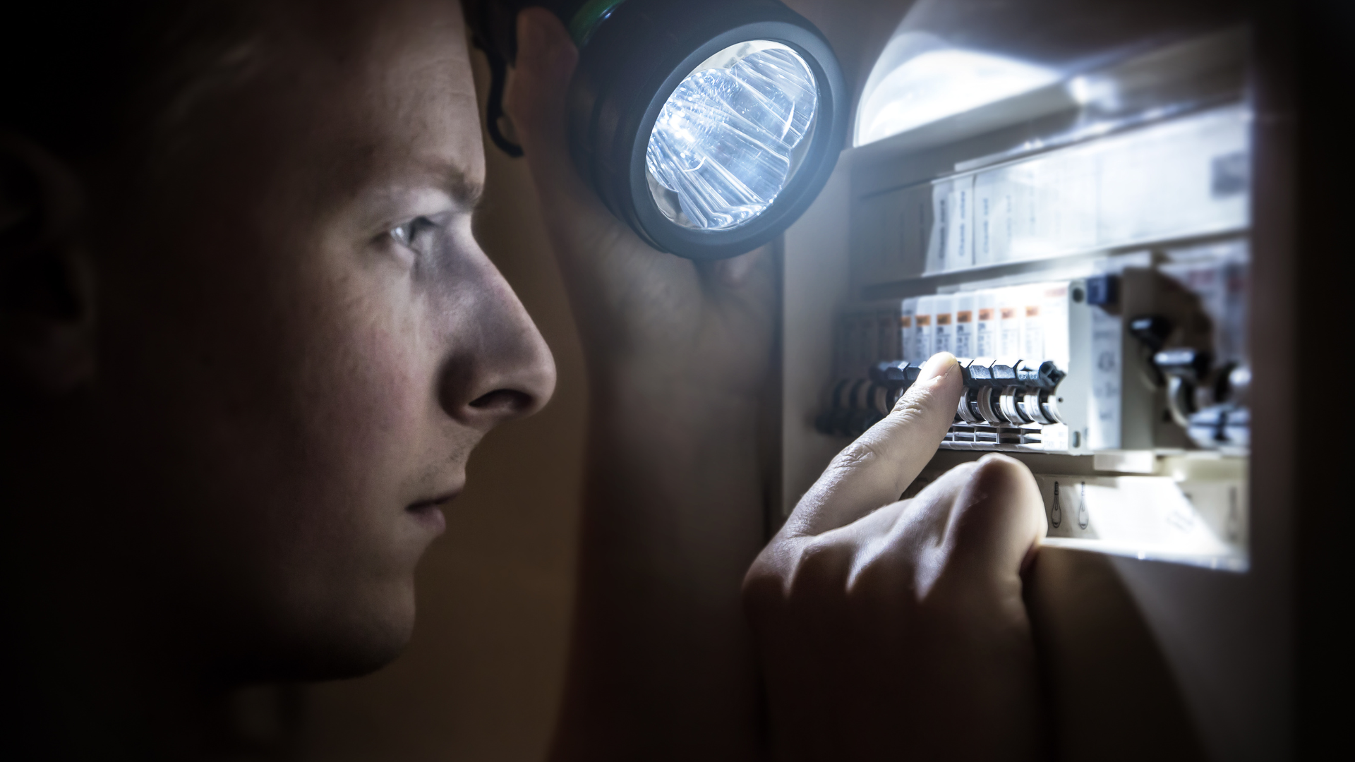 A man is looking at an electrical box with a flashlight.