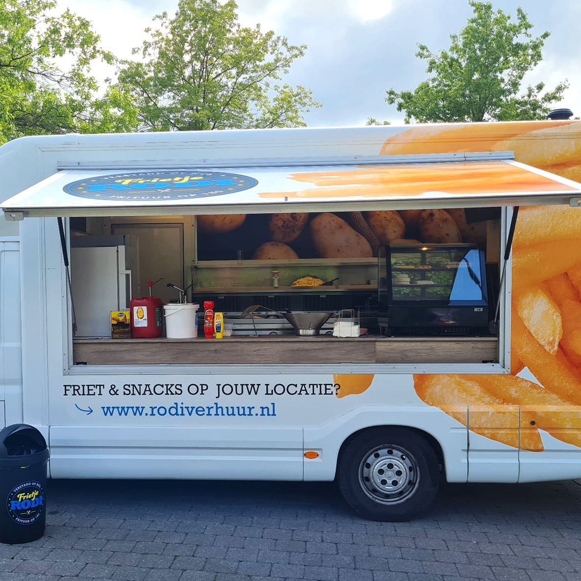 Foodtruck die friet en snacks verkoopt; witte wagen met open raam, buitenlocatie.
