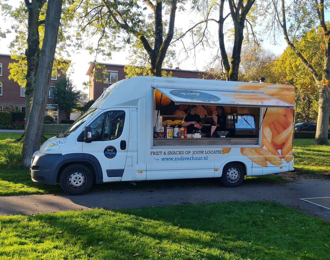 Foodtruck die frietjes verkoopt in een park, witte buitenkant, open raam, afbeelding van frietjes, zonnige dag.
