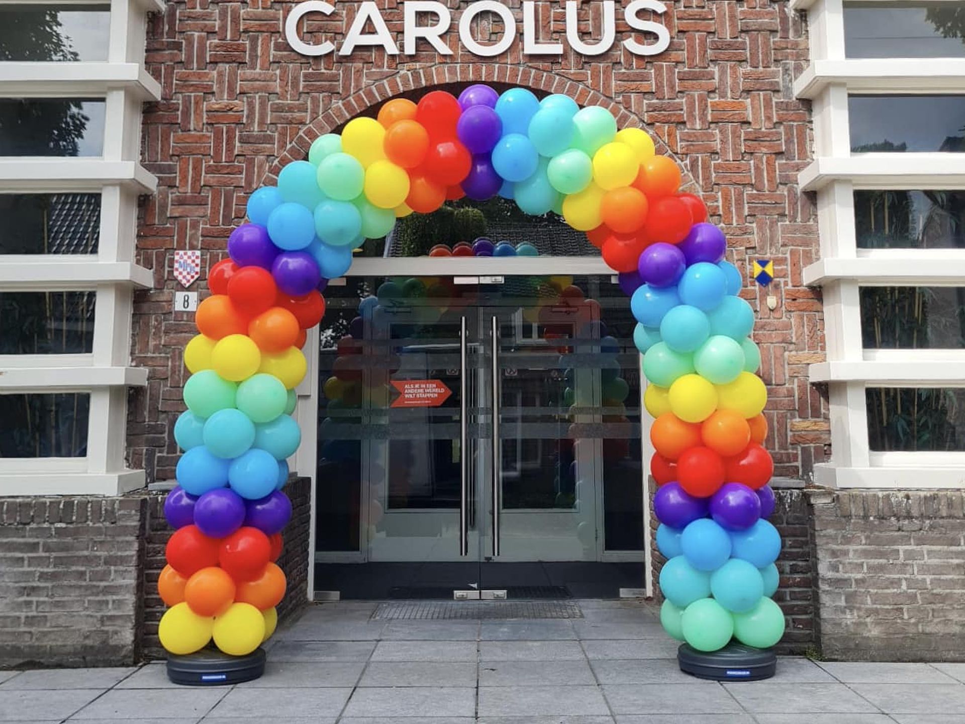 Regenboogballonnenboog bij de ingang van een gebouw met de naam
