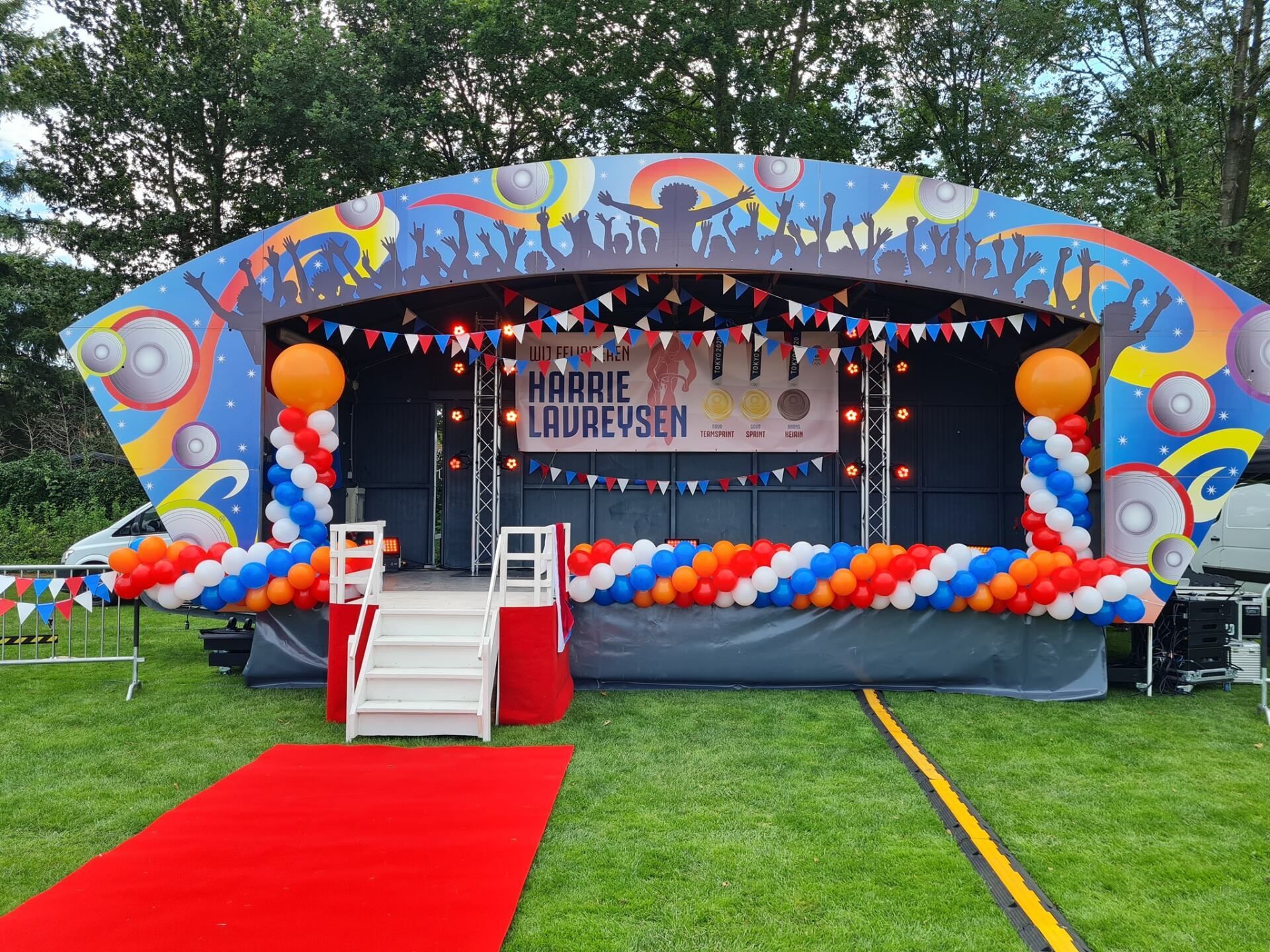 Het buitenpodium was versierd met ballonnen, slingers en een rode loper. De achtergrond was kleurrijk grafisch vormgegeven.