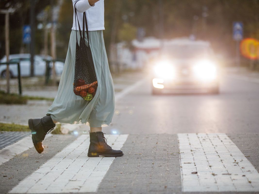 Young woman in a flowy skirt carrying mesh bag with groceries and crossing the street