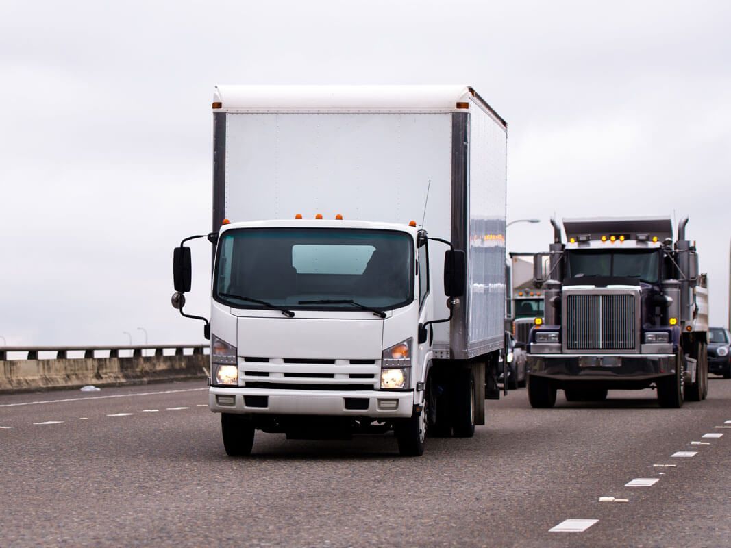 white box truck driving on highway followed by a dump truck
