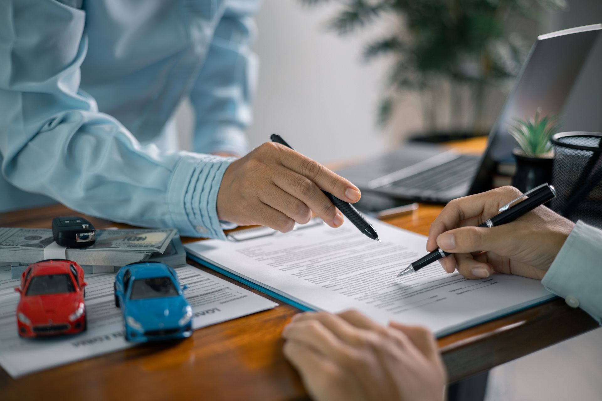 Two people reviewing and signing car insurance documents with toy cars on a desk.