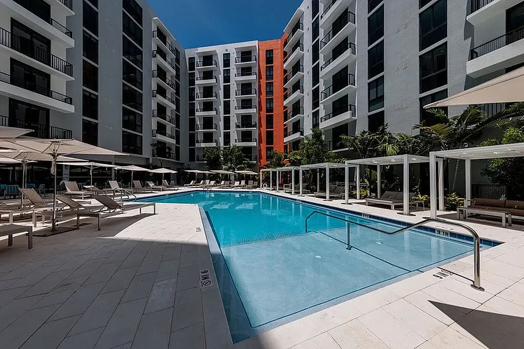 Luxurious apartment complex with modern pool area, stylish lounge chairs, and sleek architecture in a vibrant setting.