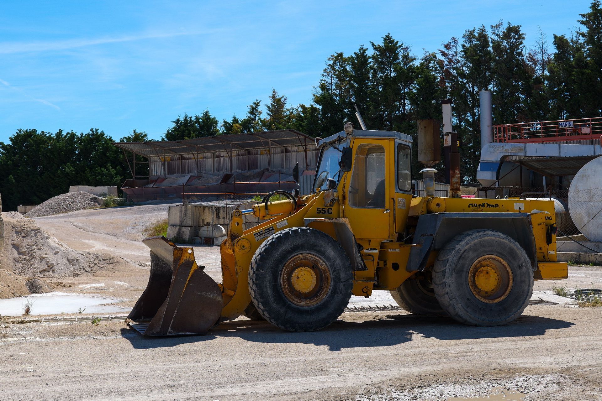 Una pala caricatrice gialla in un cantiere edile con cumuli di terra e alberi sullo sfondo preventivo asfalti Centro Beton Potenza