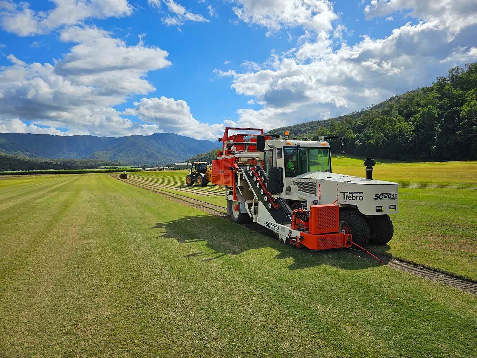 Red Farm Harvester Working in a Green Field Under a Blue, Cloudy Sky — Tropical Lawns in Mulgrave, QLD