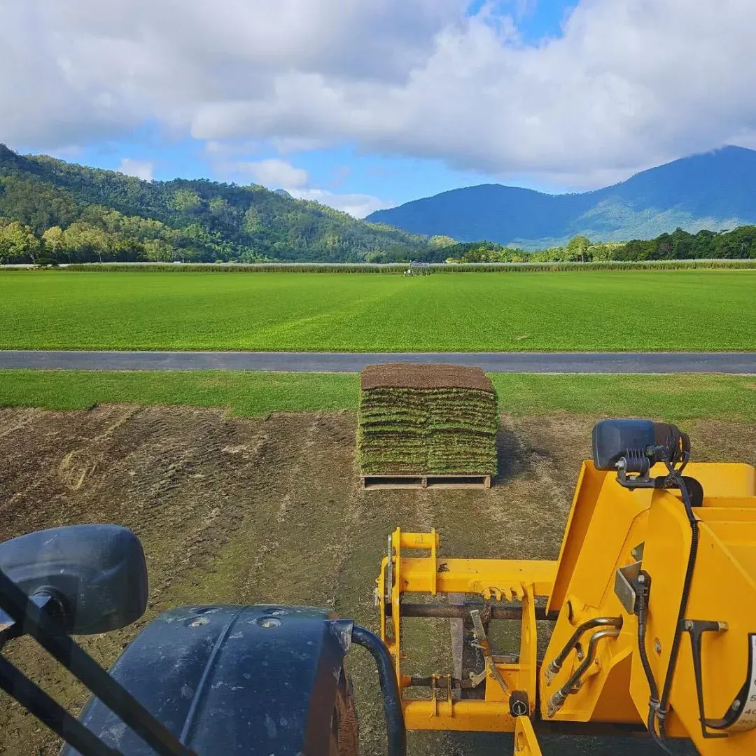 Tractor Loading Stacked Hay Bales Beside a Lush Green Field With Mountains — Tropical Lawns in Mulgrave, QLD