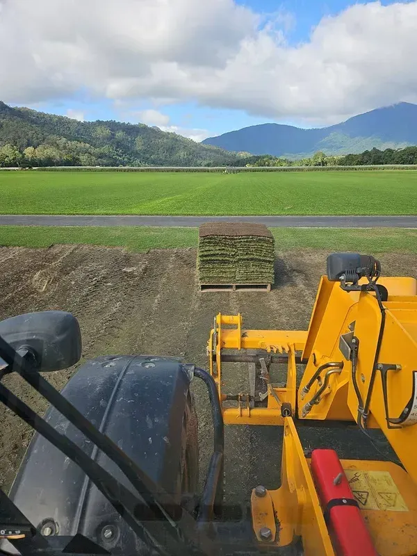 View From a Yellow Tractor Over a Green Field With Mountains and Cloudy Sky — Tropical Lawns in Mulgrave, QLD