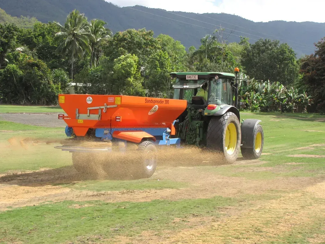 Tractor Spreading Fertilizer on a Grassy Field With Mountains in the Background — Tropical Lawns in Mulgrave, QLD