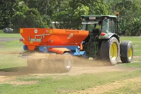 Tractor Spreading Material From an Orange Farm Implement Across a Grassy Field — Tropical Lawns in Mulgrave, QLD