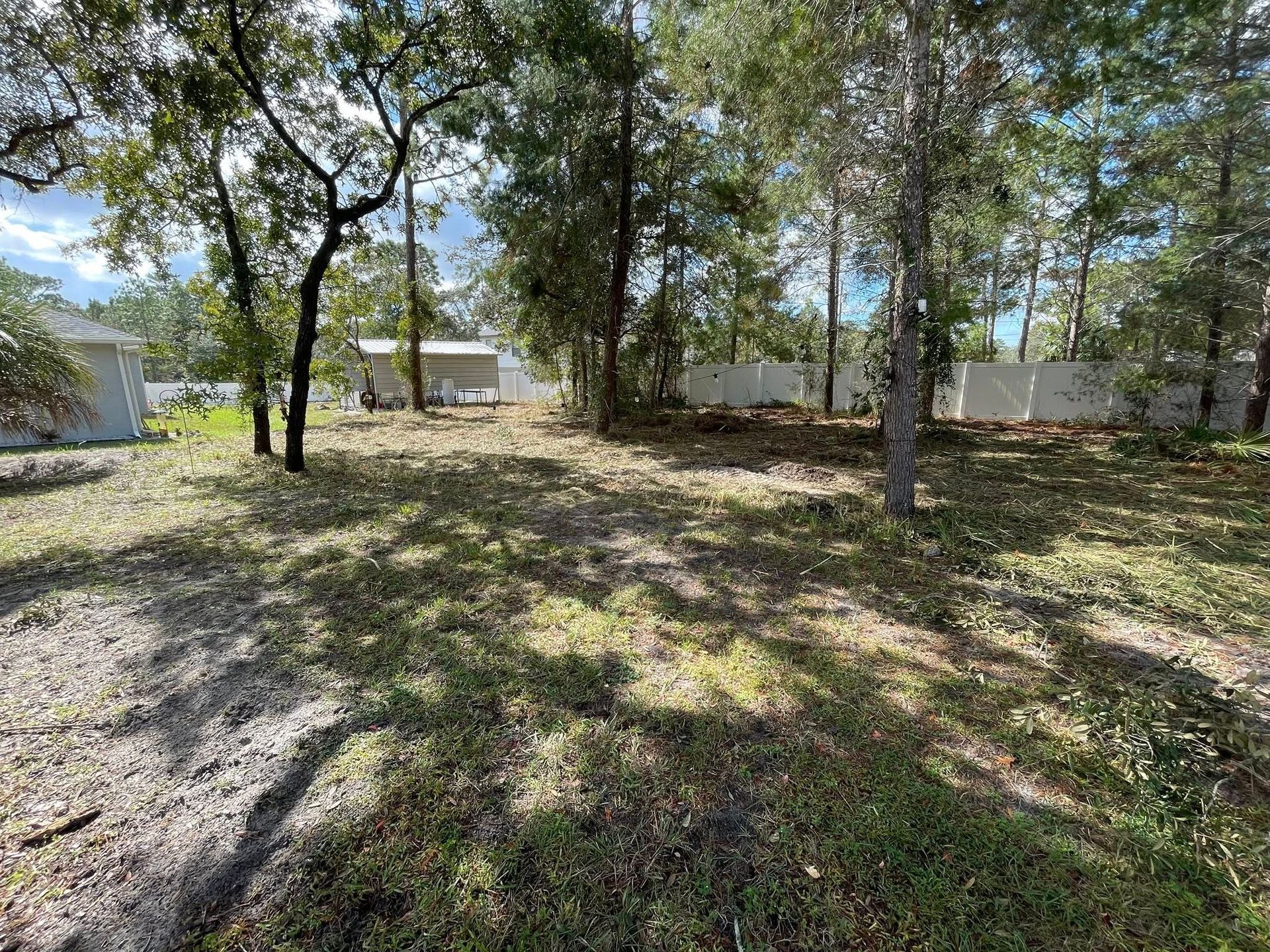 Grassy clearing with trees, white fences, and buildings in the background under a cloudy sky.