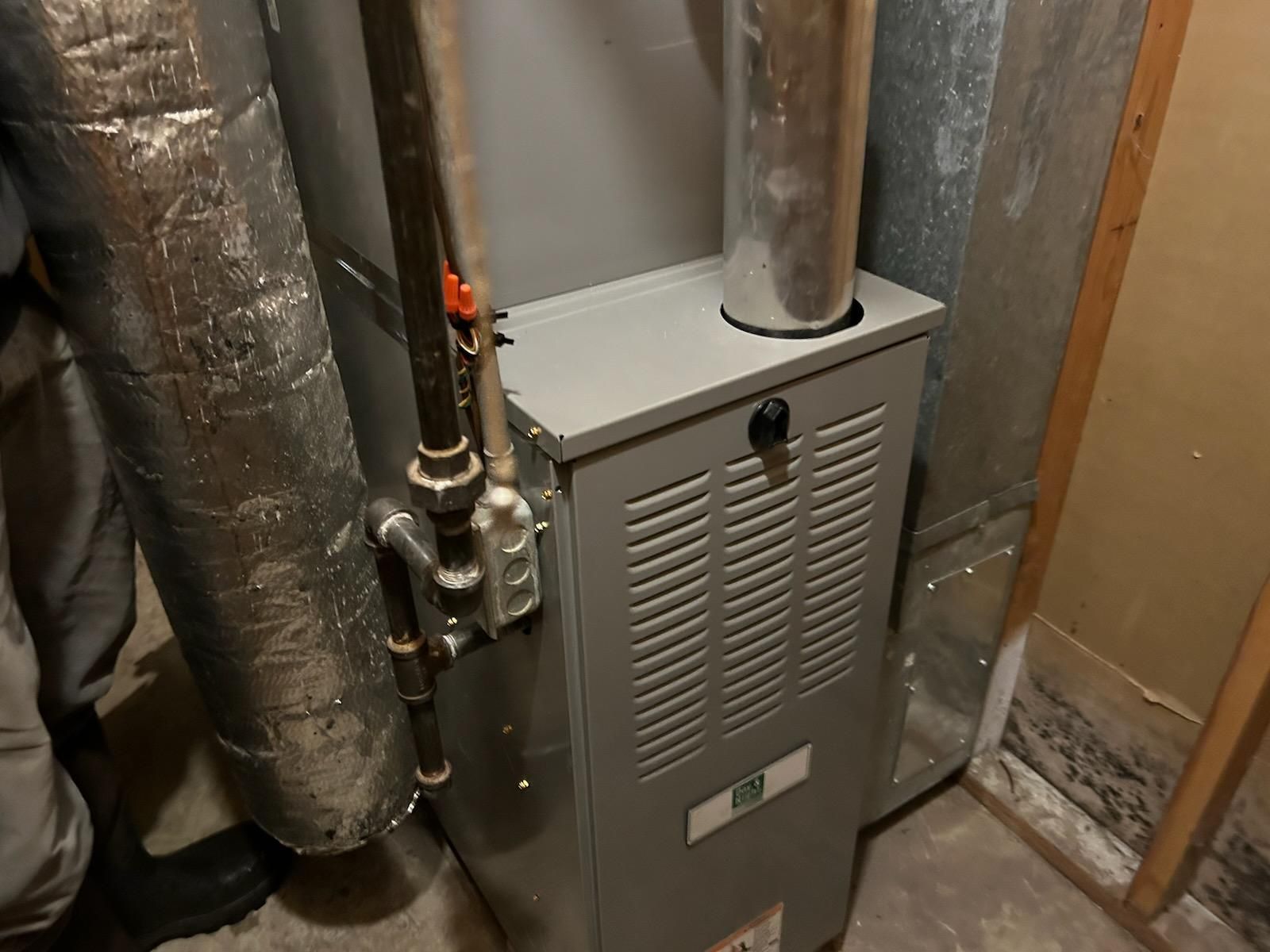 A furnace in a basement setting with silver ductwork and gas pipes.