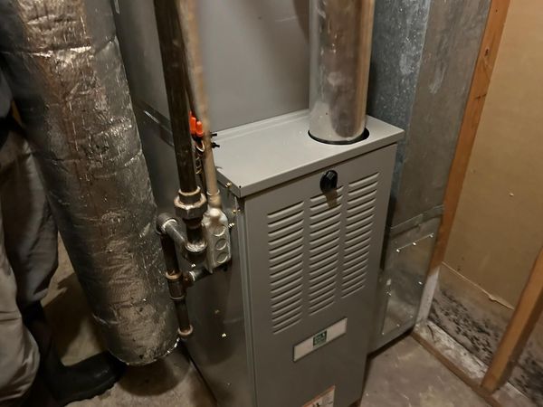 A furnace in a basement setting with silver ductwork and gas pipes.