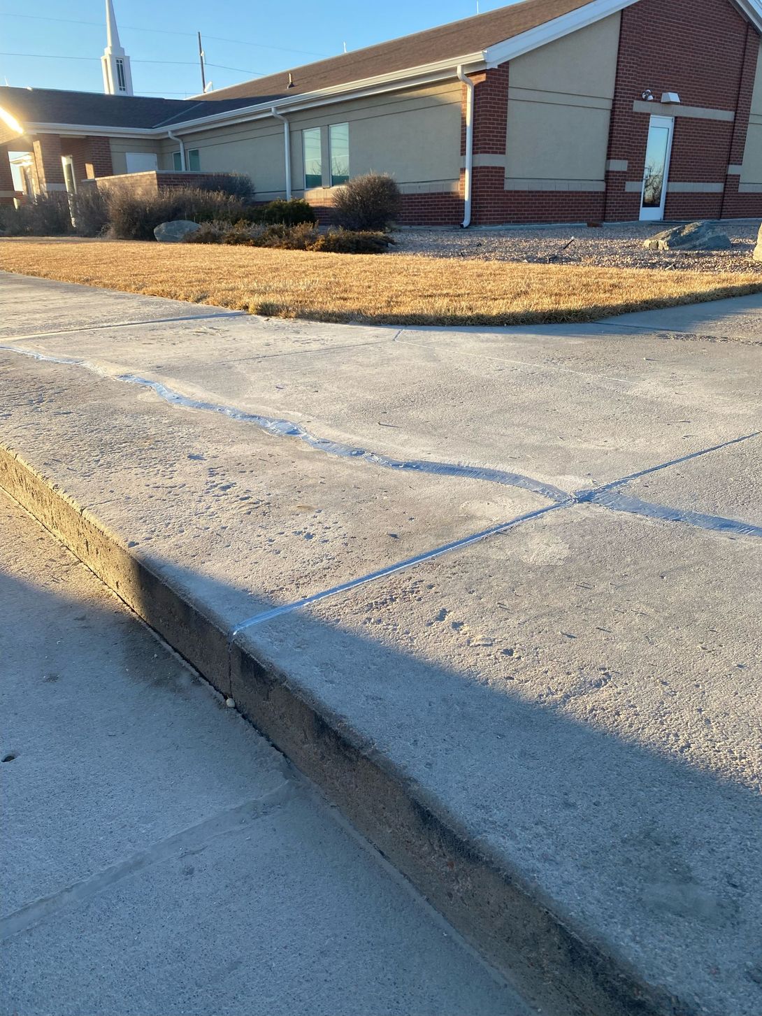 Concrete curb ramp beside a brick building with a sidewalk and dry grass in sunlight
