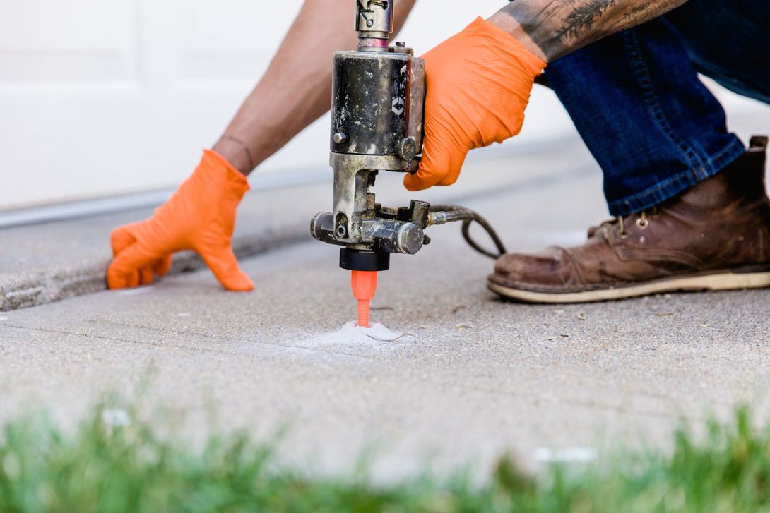 Worker using a concrete grinder on a floor, wearing orange gloves and boots.